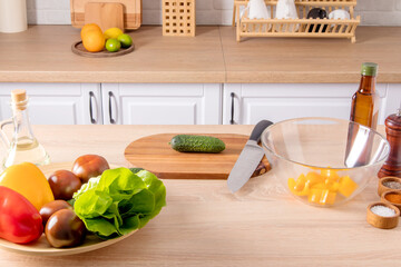 spread out on part of a modern kitchen with various items for cooking. a large dish with vegetables, a cutting board with a knife and a salad bowl.