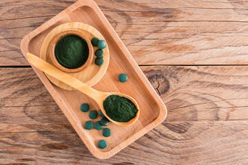 top view of the wooden table with environmentally friendly dishes filled with spirulina algae powder and green tablets. food additive.