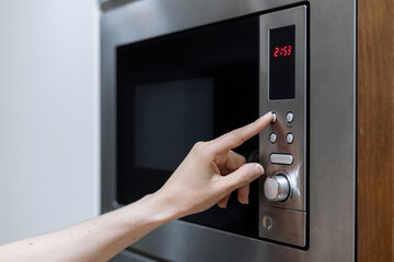 Person's hand pressing microwave oven button to start defrosting food