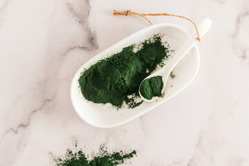 top view of a bowl of green spirulina powder on a marble white background. alternative to medicine....