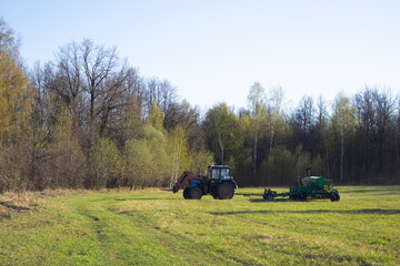 a blue tractor with a green furrow in a field against a forest background. lonely tractor