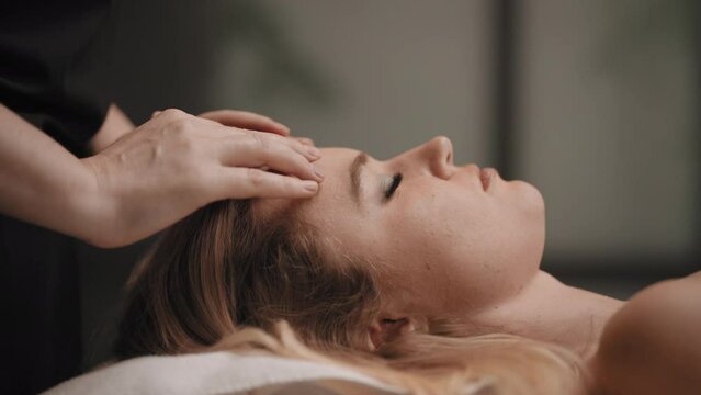 chiropractor is curing headache by massage, physician is massaging forehead of young female client