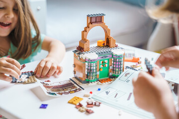 Girls, sisters play kids constructor, build house from bricks, blocks by assembly instrustions. Children activity at home in playroom. Intelligent development of fine motor skills