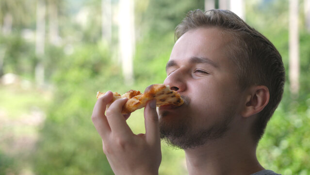 Caucasian man eating pizza. Hungry man taking a bite from pizza. Close up.