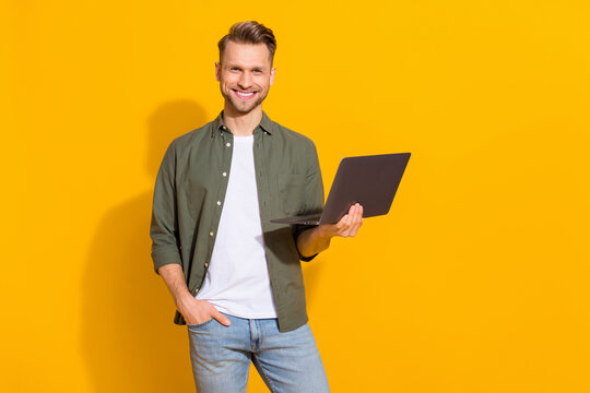 Portrait of attractive cheerful guy holding using laptop buying goods booking order isolated over bright yellow color background