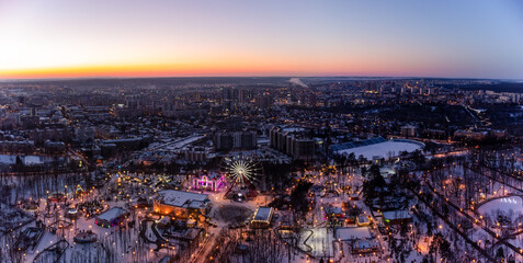 Aerial panorama view on city lights, Ferris wheel, entertainments in winter, covered in white snow. Kharkiv city center in sunset colors, amusement Gorky Central Park