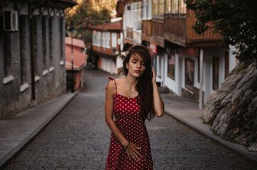 beautiful brunette girl in a red dress walks along the cobblestones in a beautiful old European town