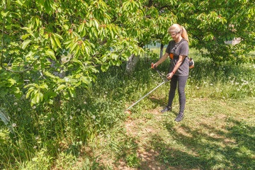 A woman mows grass on his property with a gasoline trimmer