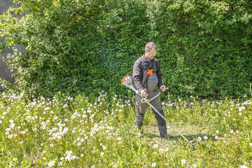 A man mows grass on his property with a gasoline trimmer