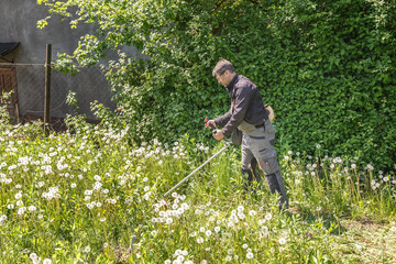 A man mows grass on his property with a gasoline trimmer