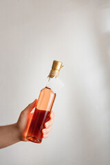 Male hand holding little glass bottle of pink rosa wine with no brand label, mock up. Vertical shot, white background, copy space