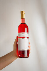 Male hand holds transparent bottle of red semisweet sweet or dry wine with no brand label, mockup template. Vertical shot, white background