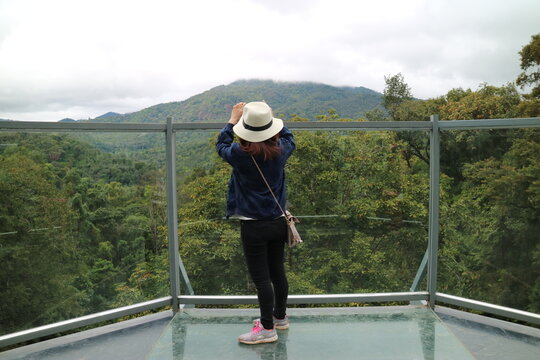 There is a female traveler standing on the observation deck looking at the distant mountain scenery and taking pictures