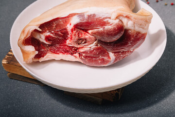 Raw pork knuckle on white plate on grey wooden background, closeup. Cooking of meat dish.