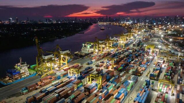 Hyper lapse time-lapse of shipping port, cargo container ship, crane, and car traffic in Asia city at night sunset. Logistic industry or freight transportation business concept, drone aerial view