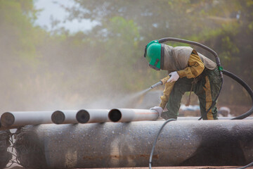 Male worker Sand blasting process cleaning pipeline surface - obrazy, fototapety, plakaty