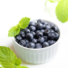 White bowl with wild forest blueberries and fresh green mint leaves on white backdrop. Superfood.