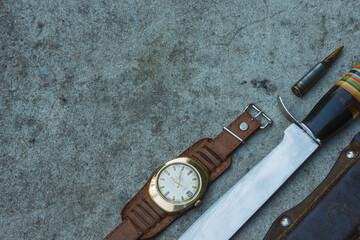 Hunting knife, leather sheath, cartridge and vintage wrist watch with leather strap lie on the concrete. Tourist equipment in outdoors. Top view.  Close-up. Copy space.