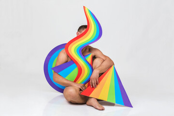 a naked man sits among various geometric shapes with a rainbow pattern, concept of LGBTQ pride,...