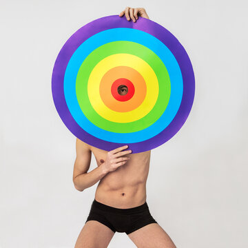 the naked young gay man looks through a hole in a rainbow target, concept of LGBTQ pride, LGBTQ people, LGBTQ rights campaign