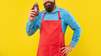 Happy man crop view in red apron holding eggplant yellow background, grocer