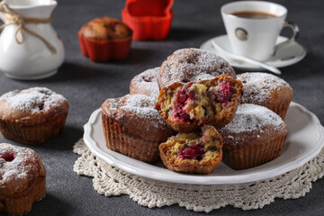 Muffins with cherries sprinkled with powdered sugar on a white plate on dark background. Close-up
