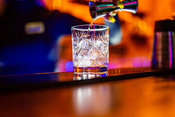 woman bartender hand pours alcohol in glass with ice in nightclub