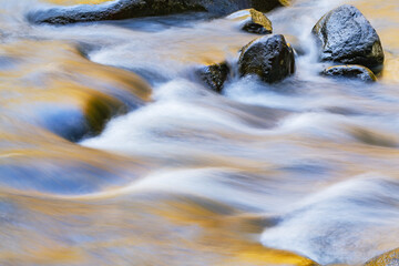 Fototapeta na wymiar Landscape of the Little River captured with motion blur and aglow with reflected color from sunlit autumn foliage, Great Smoky Mountains National Park, Tennessee, USA