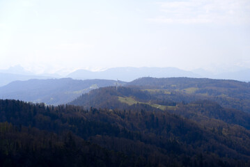 Obraz premium Panoramic view from local mountain Uetliberg with valley, village, agricultural fields and Swiss Alps in the background on a blue cloudy spring day. Photo taken April 14th, 2022, Zurich, Switzerland.