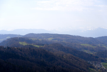 Panoramic view from local mountain Uetliberg with valley, village, agricultural fields and Swiss Alps in the background on a blue cloudy spring day. Photo taken April 14th, 2022, Zurich, Switzerland.