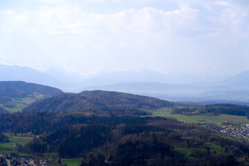 Fototapeta na wymiar Panoramic view from local mountain Uetliberg with valley, village, agricultural fields and Swiss Alps in the background on a blue cloudy spring day. Photo taken April 14th, 2022, Zurich, Switzerland.