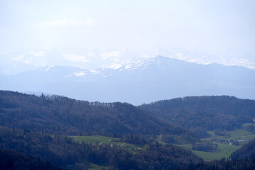 Panoramic view from local mountain Uetliberg with valley, village, agricultural fields and Swiss Alps in the background on a blue cloudy spring day. Photo taken April 14th, 2022, Zurich, Switzerland.