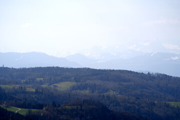 Panoramic view from local mountain Uetliberg with valley, village, agricultural fields and Swiss Alps in the background on a blue cloudy spring day. Photo taken April 14th, 2022, Zurich, Switzerland.