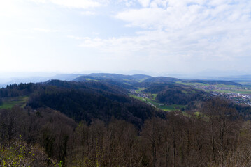 Fototapeta na wymiar Panoramic view from local mountain Uetliberg with valley, village, agricultural fields and Swiss Alps in the background on a blue cloudy spring day. Photo taken April 14th, 2022, Zurich, Switzerland.