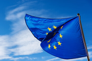 Close-up of a European Union flag waving against a clear blue sky with clouds and copy space.

