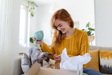 Female consumer unpack parcel receive retail purchase fast postal shipping delivery concept. Beautiful young woman is holding cardboard box sitting on sofa at home.