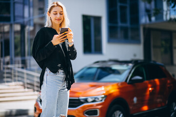 Fototapeta premium Woman using phone in the street by the car