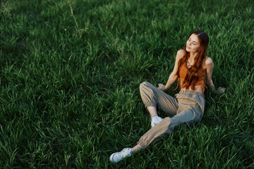 Fototapeta premium A girl sits on the grass in the park and enjoys the beautiful view of the summer sunset