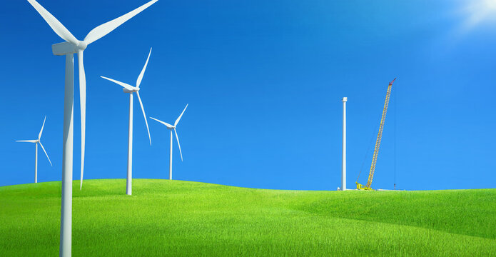 Windfarm in a field of green grass with construction crane installing new wind turbine against blue sky