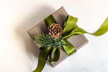 Overhead close-up of a gift box decorated with a green ribbon, fir sprig and pinecone