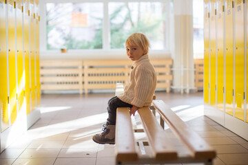 Sweet blonde toddler boy standing in front of a lockers in kindergarden or school hallway