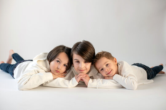 Cute stylish toddler child and older brothers, boys with white shirts on white background, family kids portrait