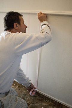 Painter attaching masking tape to a wall from the dado rail to the floor in preparation for painting stripes