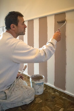 Painter painting stripes on a wall below a dado rail with a roller