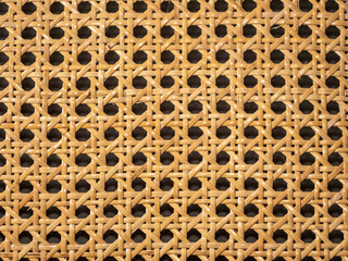 Image en gros plan d’un cannage traditionnel en rotin naturel, présentant un motif géométrique...