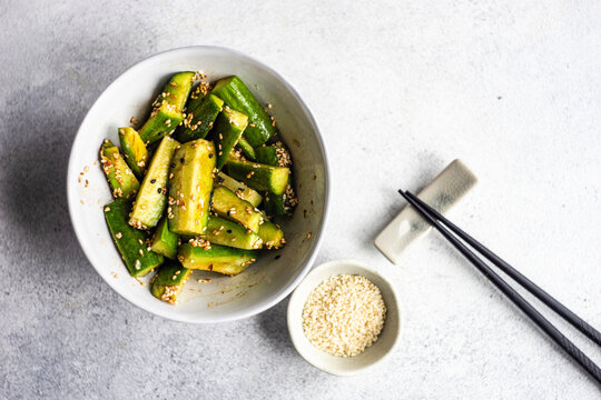 Overhead view of a bowl of spicy Asian cucumber salad with sesame seeds and chopsticks