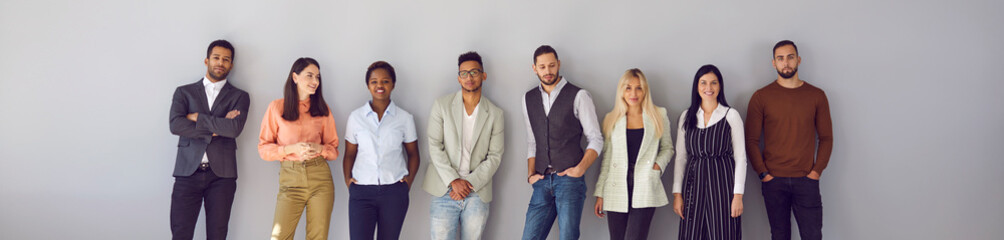 Young diverse fashion models posing against gray background. Banner with group portrait of confident young multi ethnic people in smart casual office wear standing in studio and leaning on grey wall - Powered by Adobe