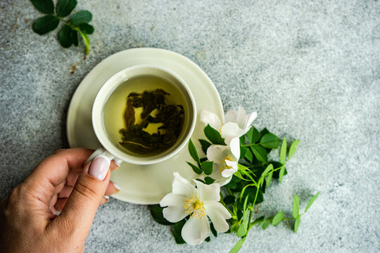Woman reaching for a cup of green tea and white wild rose flowers on a table