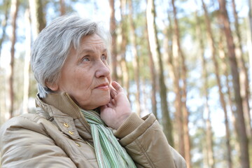 Portrait of pensive senior woman walking in the forest in autumn