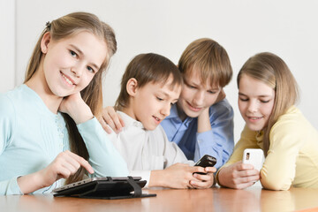 Portrait of funny boys and girls using digital devices together at the table at home